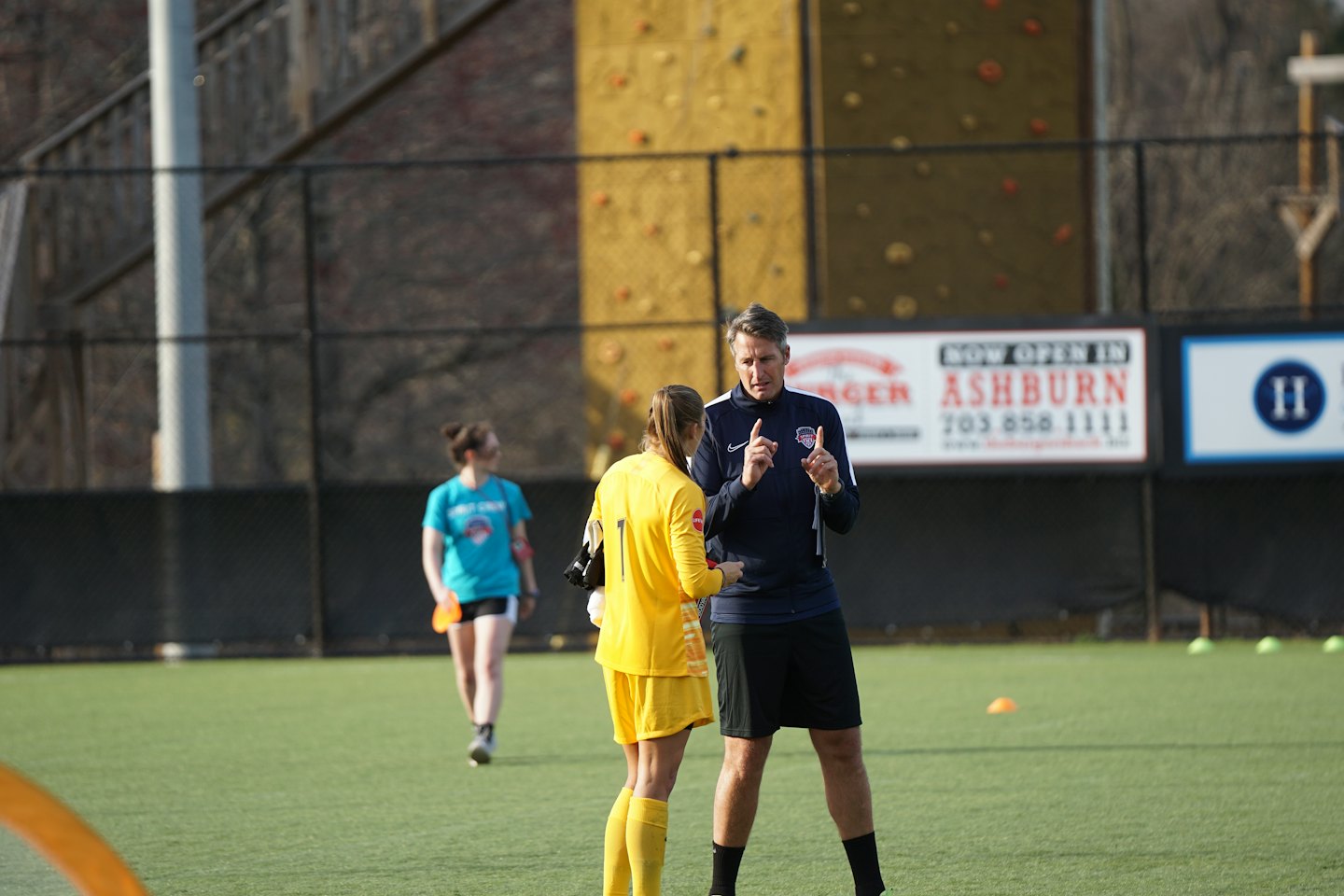 Allenatore istruisce giovane calciatrice su erba sintetica.