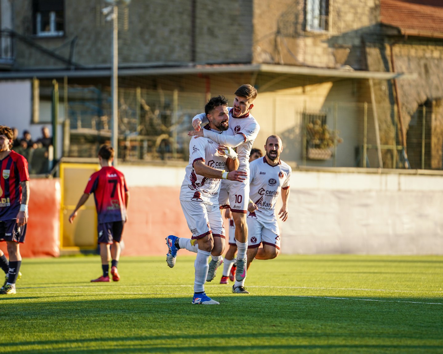 Due calciatori festeggiano gioiosamente su un campo verde soleggiato.
