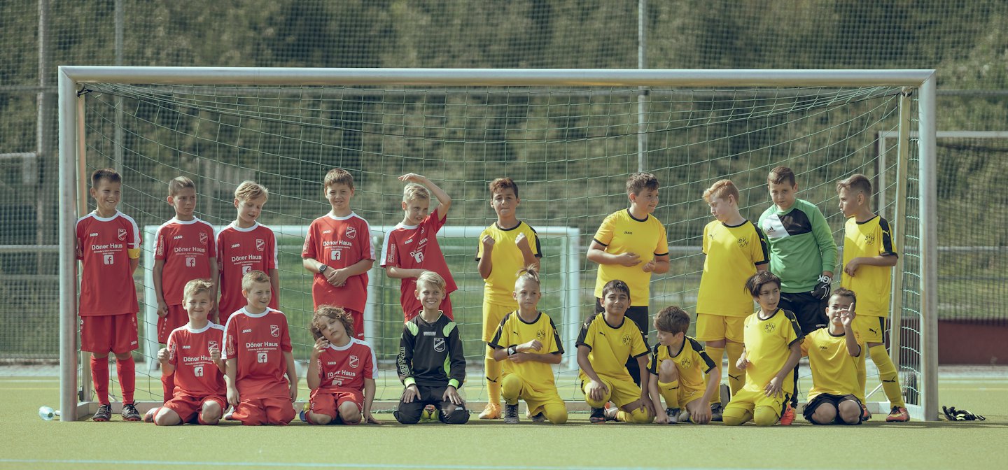 Squadra di calcio giovanile in divisa rossa e gialla posa sul campo.