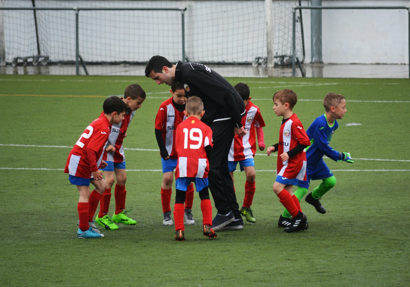Allenatore di calcio che istruisce ragazzini su un campo in erba sintetica.
