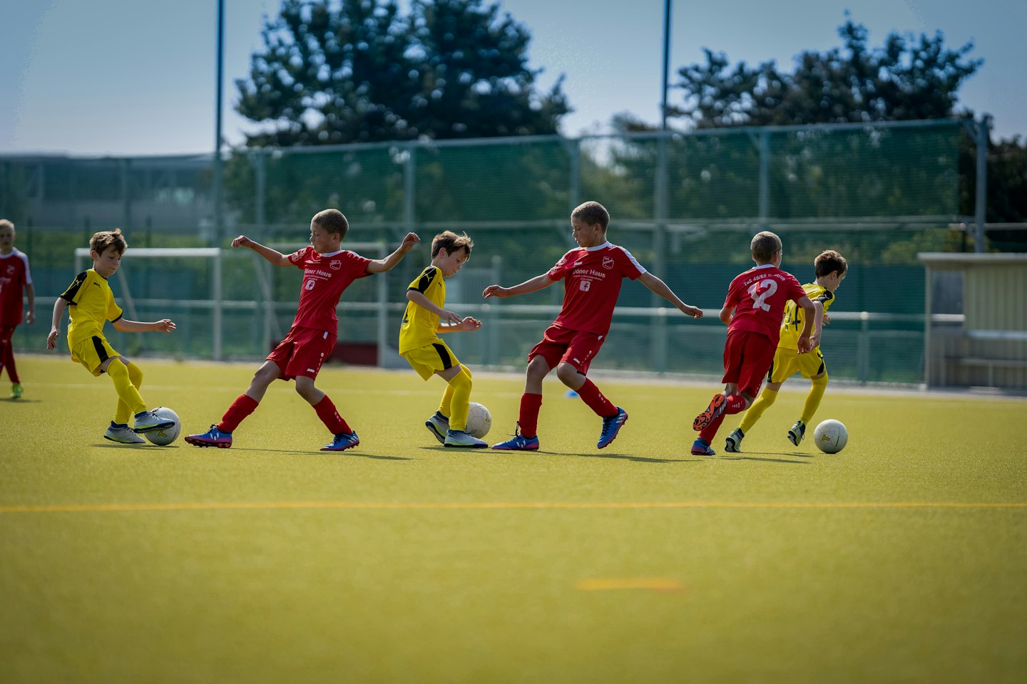 Ragazzi in divisa da calcio rossa e gialla giocano su un campo verde.